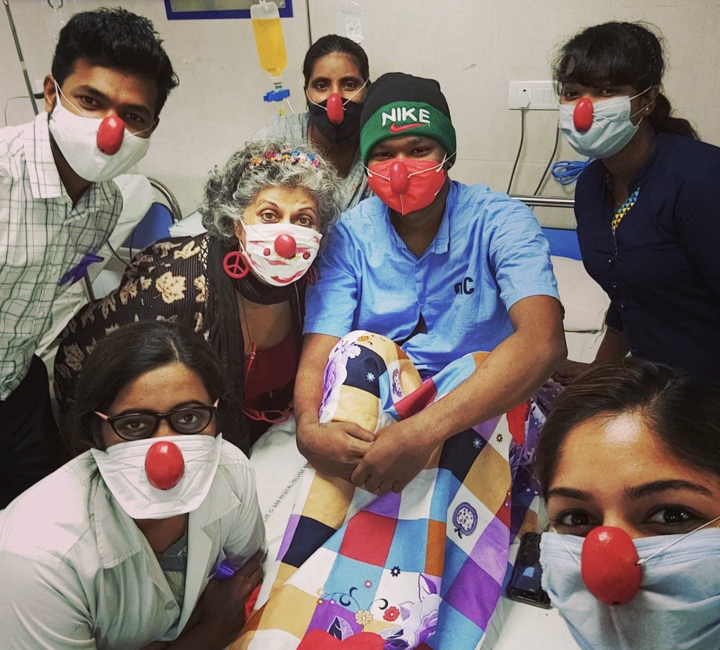 Volunteers wearing red clown noses with a young patient on the ward