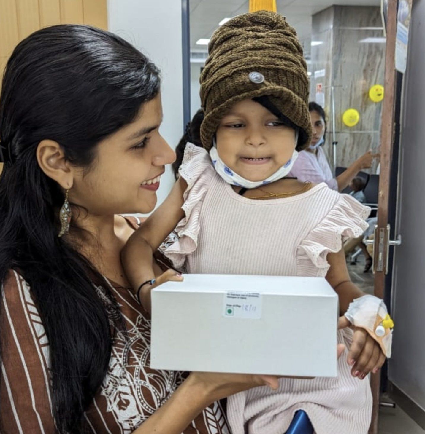 A Sabrcare volunteer holding a smiling young patient with a gift box