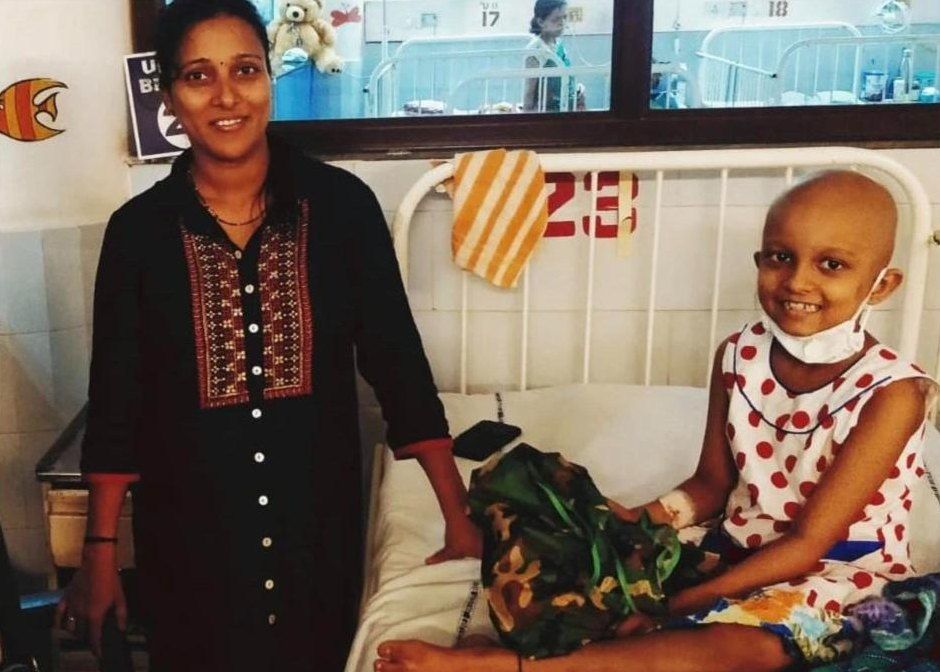 A smiling child on a hospital bed beside a Sabrcare volunteer