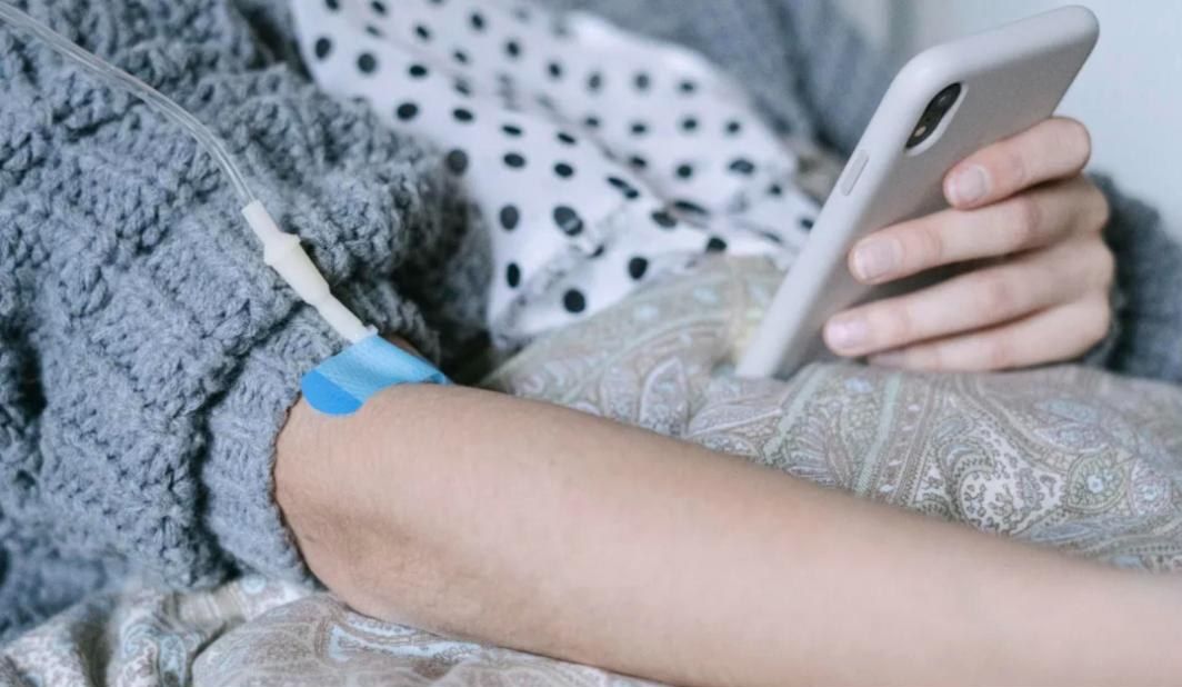 A patient’s hand holding a phone, with an IV line taped to the arm