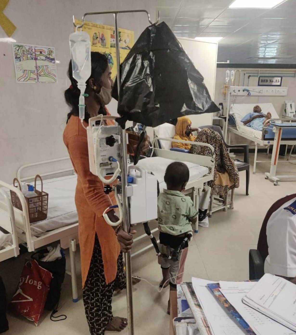 A mother walks with her young child and his drip stand on the hospital ward