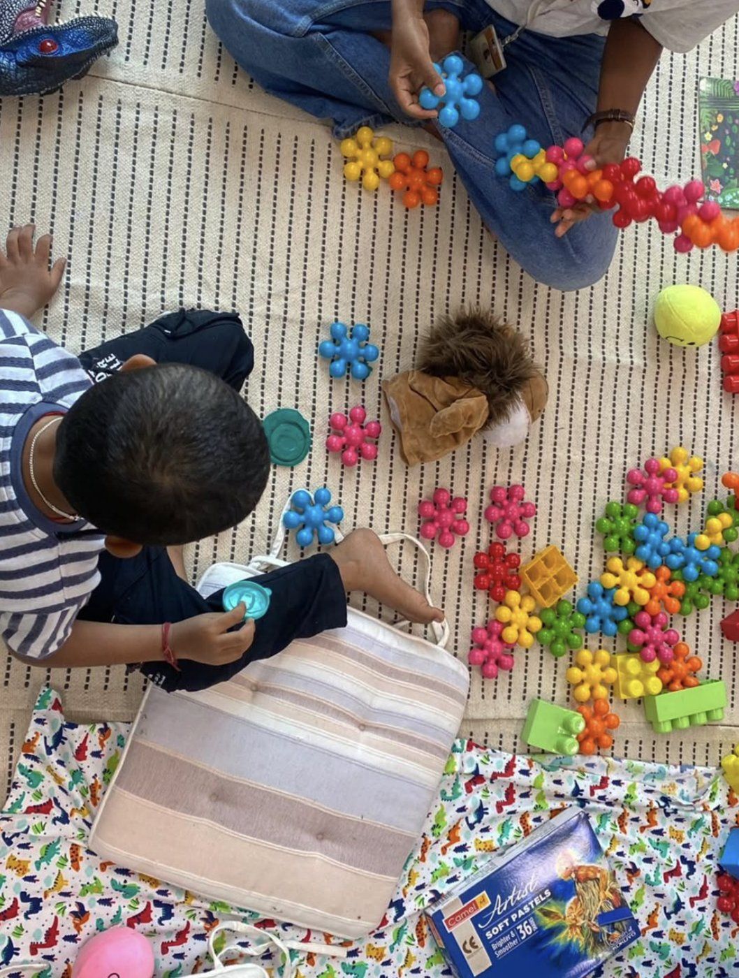Seen from above, a child plays with colourful building blocks on a floor mat