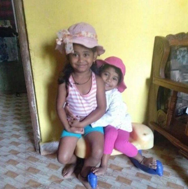 Raziel and her little sister smiling in sun hats at home